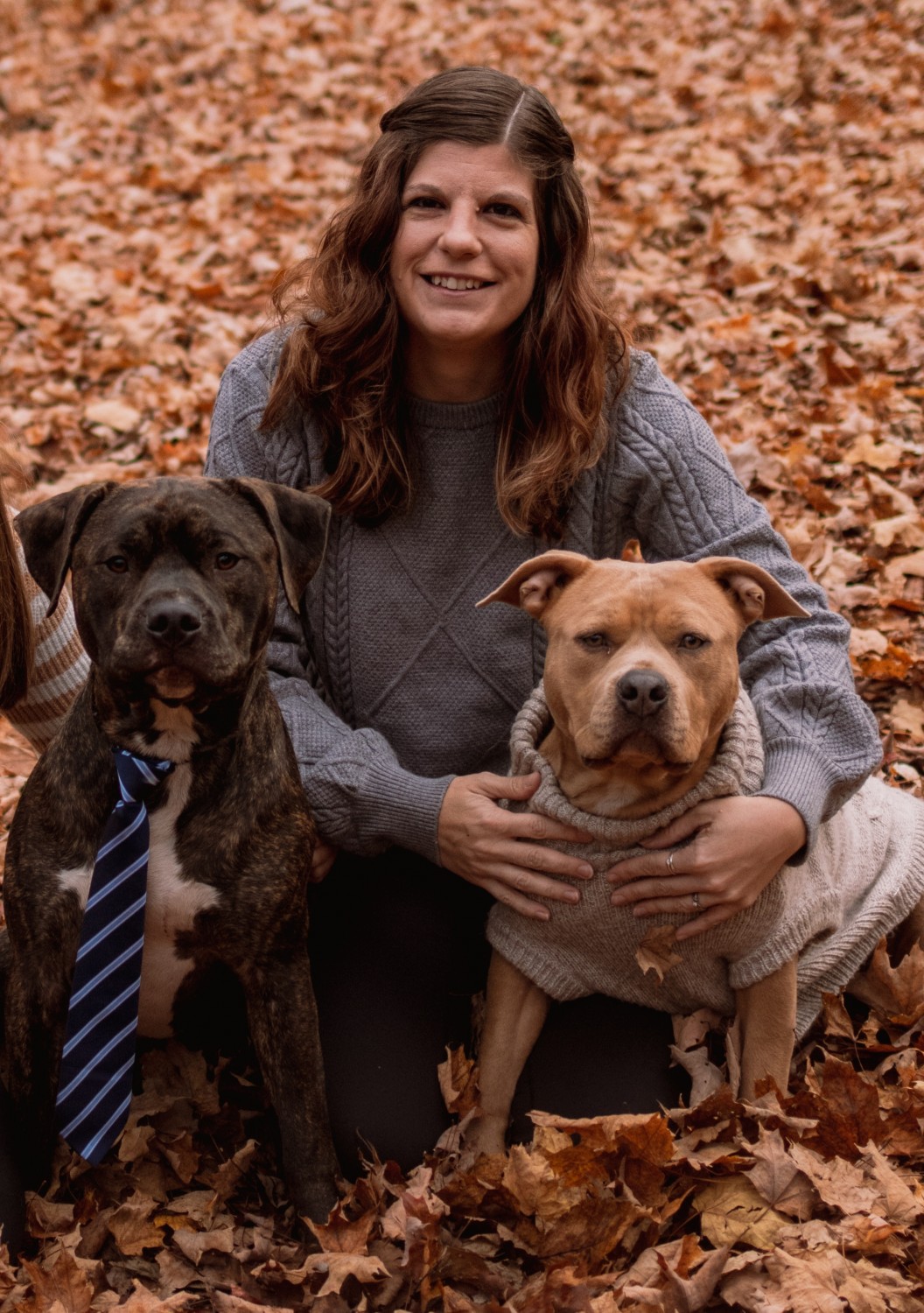A picture of a dark-haired woman and two dogs in autumn leaves.